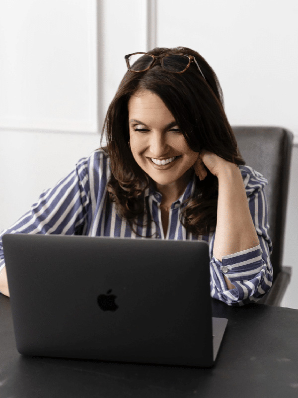 A smiling woman working on a laptop at her desk, casual office environment, Ocean City Moms.