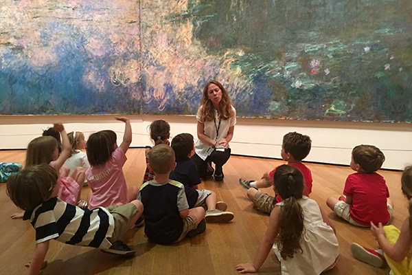 A colorful art gallery with children listening to a woman explaining artwork.