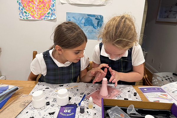 A woman and a girl doing a nail art craft at a table with nail polish bottles and tools.